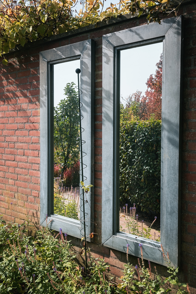 Twee tuinspiegels die aan een muur in een tuin zijn gehangen